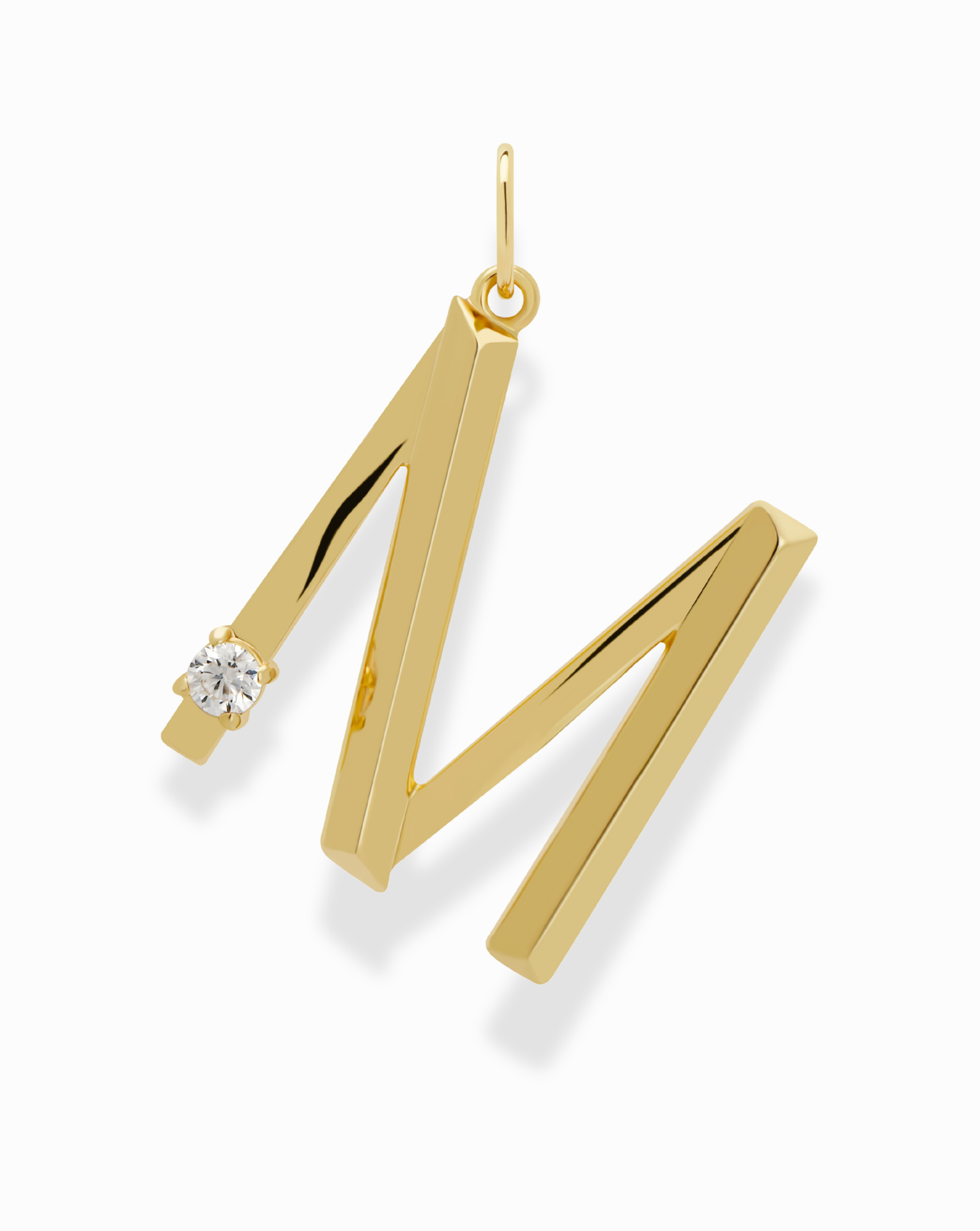 The Eloise Letter Charm by Mod + Jo is a gold pendant shaped like the letter M, accented with a sparkling cubic zirconia on the upper left side, shown against a white background.