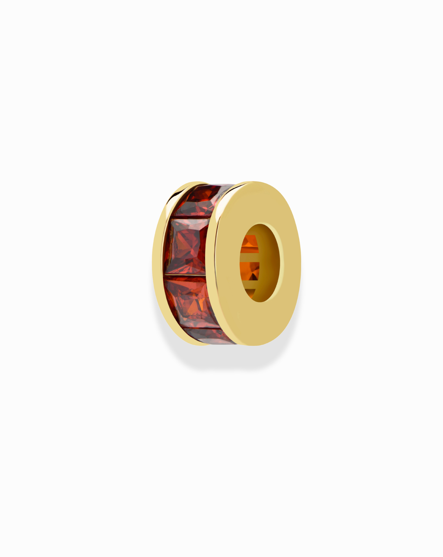 The Mod + Jo Este Birthstone Charm Spacer is a gold spacer bead with a hollow center and a row of rectangular red gemstones, ideal for personalizing your jewelry collection. Displayed on a white background.