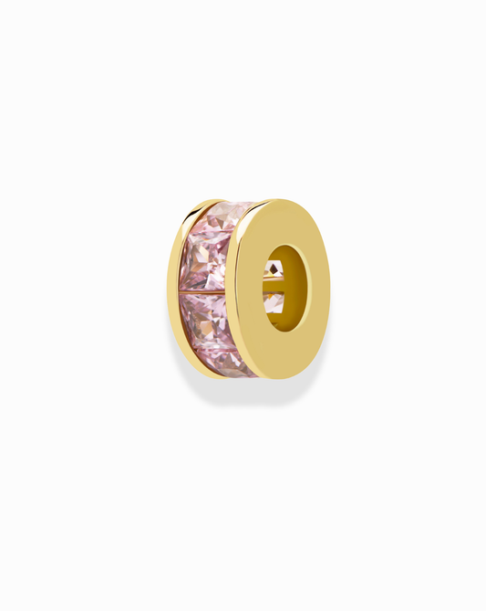 The Mod + Jo Este Birthstone Charm Spacer is a gold necklace spacer with a hollow center and a row of pink gemstones, perfect for adding color to any personalized necklace. Shown on a white background.