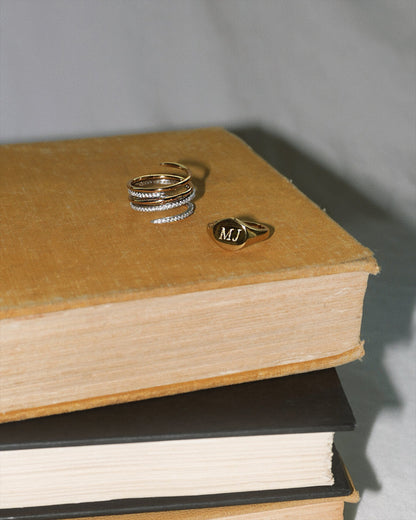 Tessa Signet Ring displayed alongside a stackable ring on a vintage book, showcasing jewelry style and personalization.