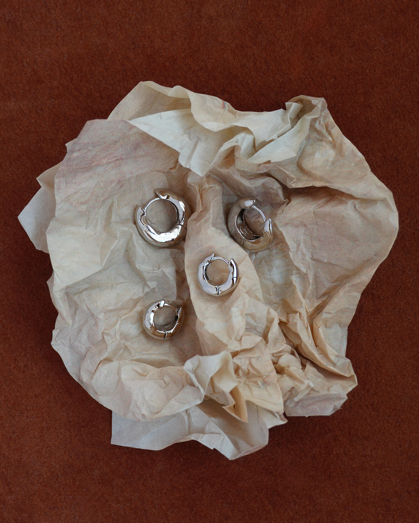 Silver hoop earrings on crumpled beige tissue paper against a brown background