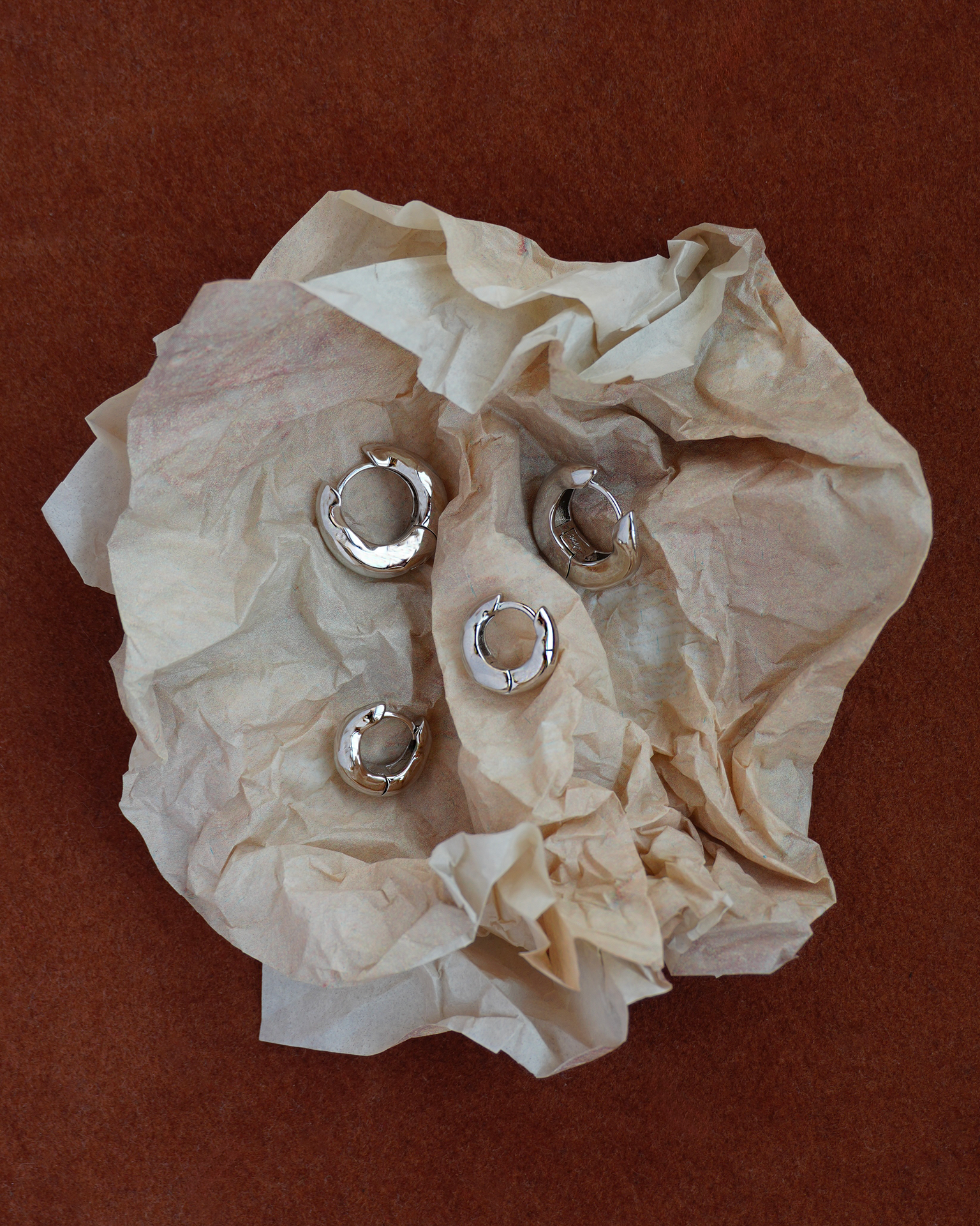 Silver hoop earrings on crumpled beige tissue paper against a brown background