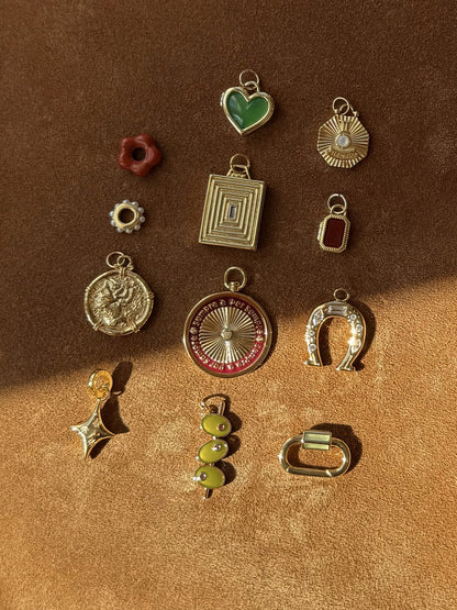 The Minka Enamel Swivel Charm by Mod + Jo features assorted gold and colorful charms—14k gold plate horseshoe, compass, heart, star, beads, and geometric designs—nickel- and lead-free—displayed on brown suede in sunlight.