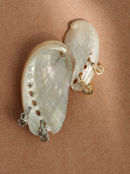 Two iridescent abalone shells display Mod + Jo’s *Preorder* Levi Huggies—one pair in gold, the other in tarnish-resistant silver—perfect for a modern lobe stack on a textured surface.