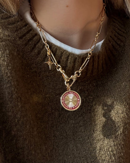 A close-up of a person wearing the Mod + Jo Minka Enamel Swivel Charm, a 14k gold plate chain necklace with a round red and white pendant and star charm over a brown sweater and white shirt. Nickel- and lead-free for safe, comfortable wear.