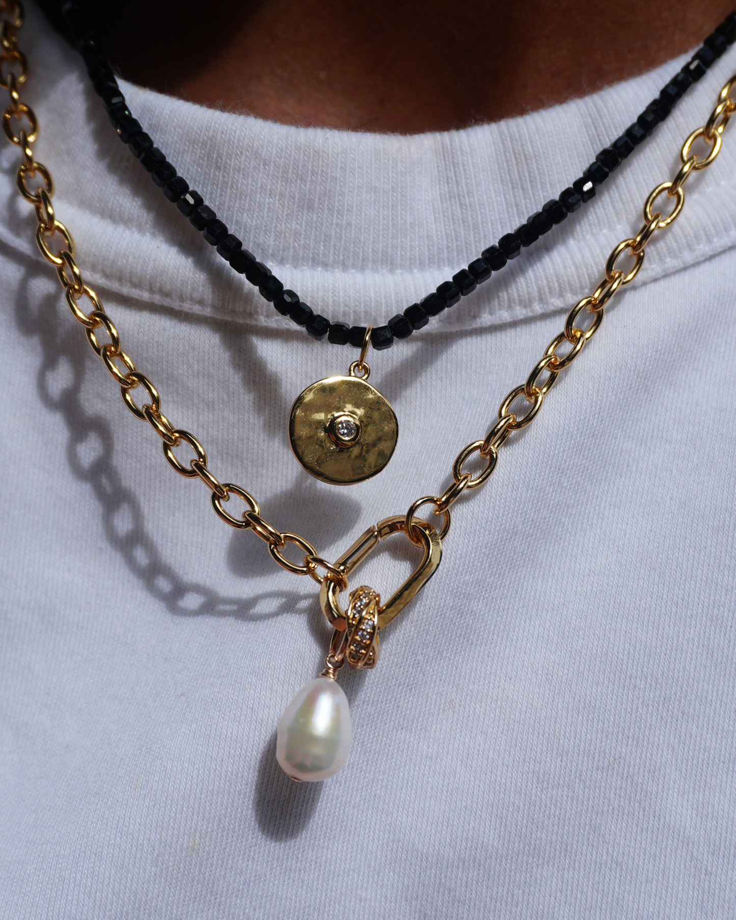 Amber Knife Edge Enhancer necklace shown on a model. Layered gold chain with pearl charm and black beaded strand.