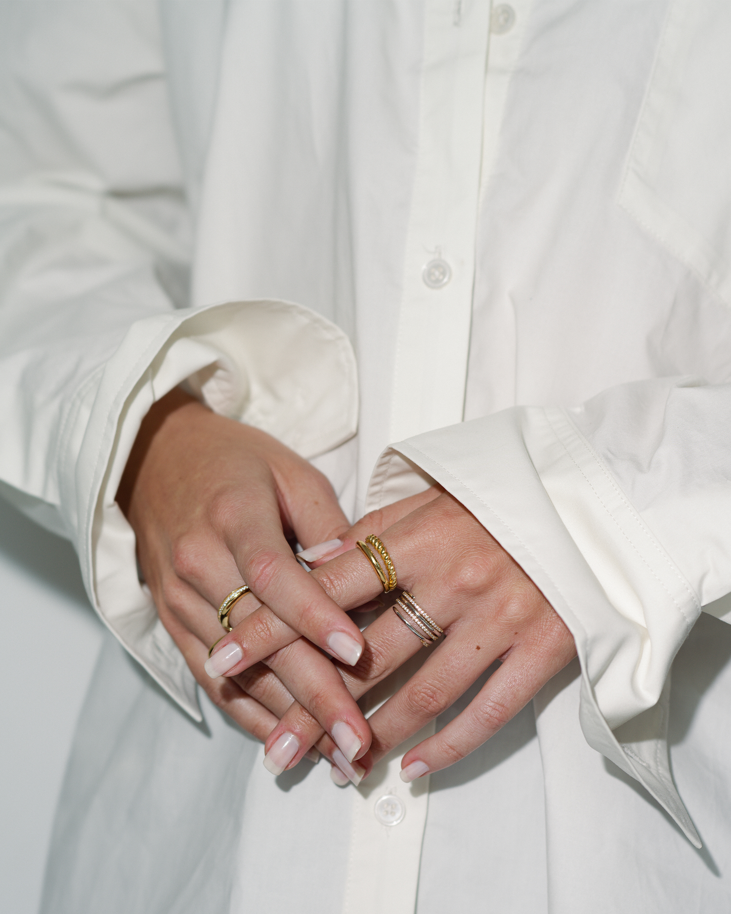 Close-up of hands wearing gold rings with a white shirt background