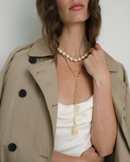 Model wearing Portia gemstone necklace with a gold lariat layered over a bead necklace, styled with a trench coat.