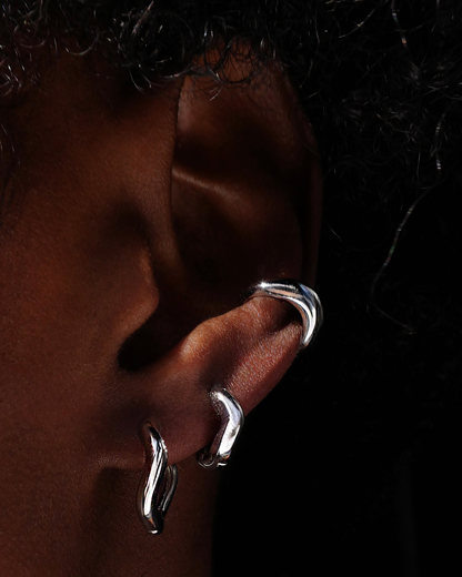 Silver wavy hoops and ear cuff on an ear with a dark background