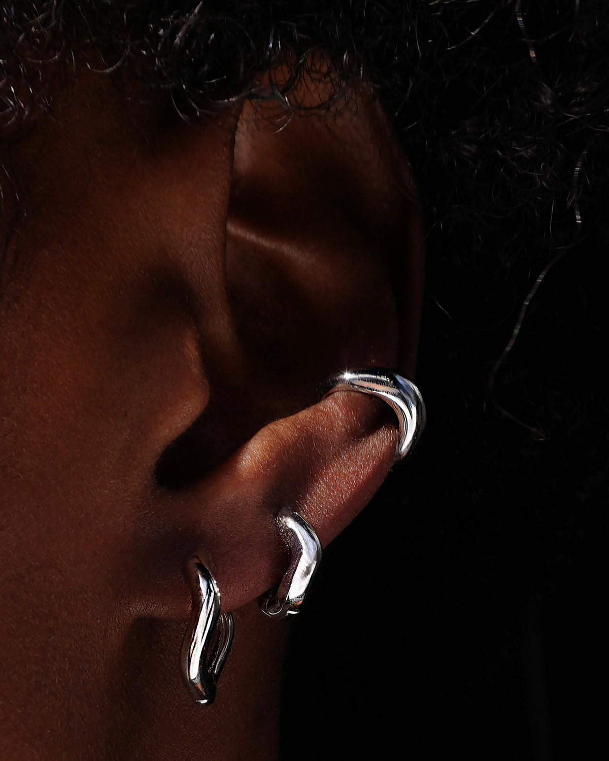 Silver wavy hoops and ear cuff on an ear with a dark background