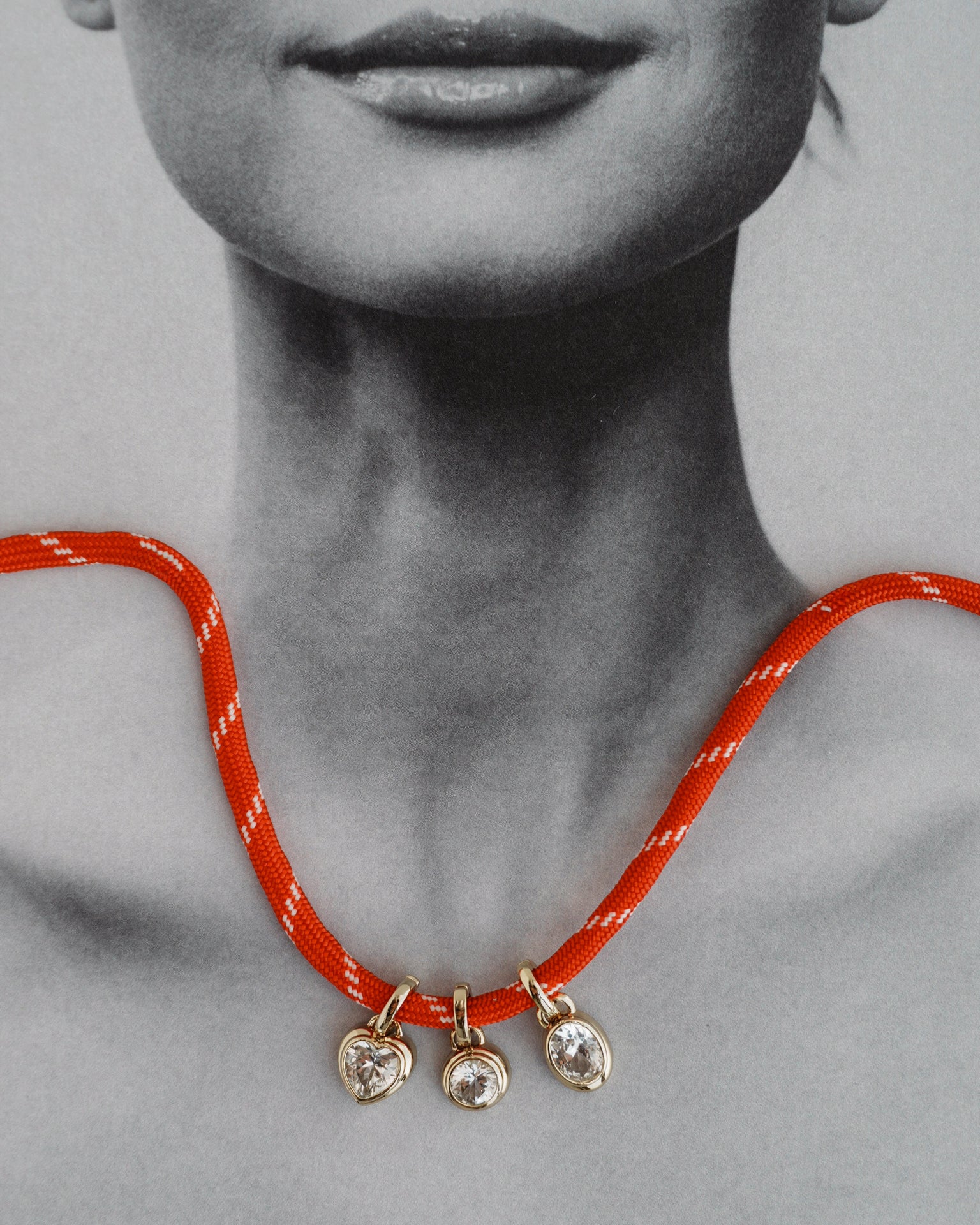 The Mod + Jo Jovie Sapphire Heart Charm necklace is draped over a black and white photo of a woman's lower face and neck, making it appear as if she is wearing the elegant piece.