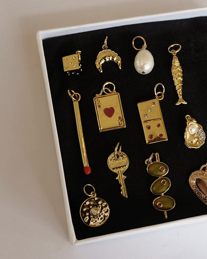 Gold Jenna Dice Charm, along with croissant, key, heart & other luxury-themed jewelry charms showcased in a box.