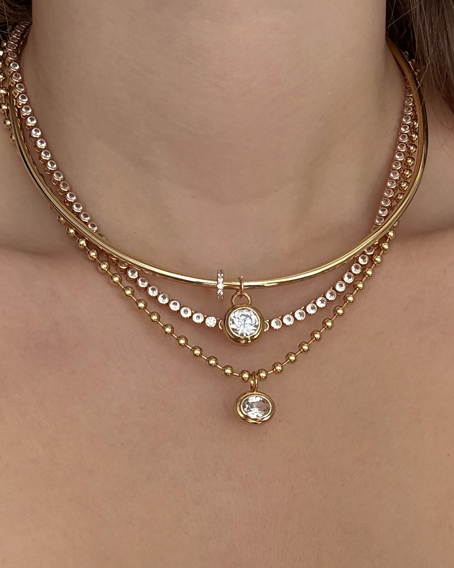 A close-up of a woman's neck wearing Mod + Jo's Leah Pave Charm Spacer—a layered gold plate necklace with clear cubic zirconia accents—for an elegant, stacked jewelry look.