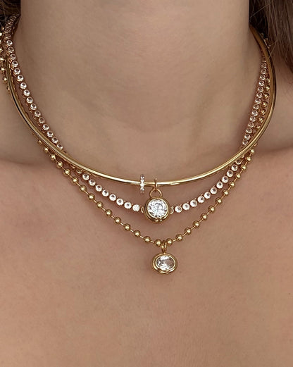 A close-up of a woman's neck wearing Mod + Jo's Leah Pave Charm Spacer—a layered gold plate necklace with clear cubic zirconia accents—for an elegant, stacked jewelry look.
