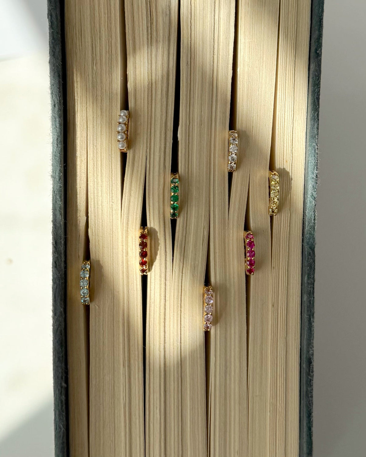 The Mod + Jo Harlow Reversible Birthstone Huggies are displayed between the pages of an open book, with soft natural light casting gentle shadows on the pages.
