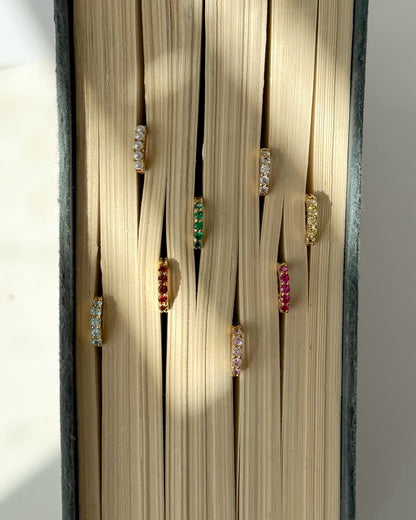The Mod + Jo Harlow Reversible Birthstone Huggies are displayed between the pages of an open book, with soft natural light casting gentle shadows on the pages.