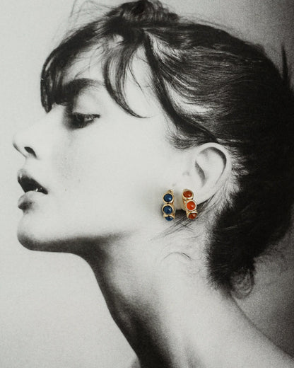 Black and white side profile of a woman wearing Mod + Jo’s Corynn Gemstone Huggies—blue and natural red agate stones set in 18k gold plating. Her dark hair is in a bun, head tilted back to highlight her neck and jawline.