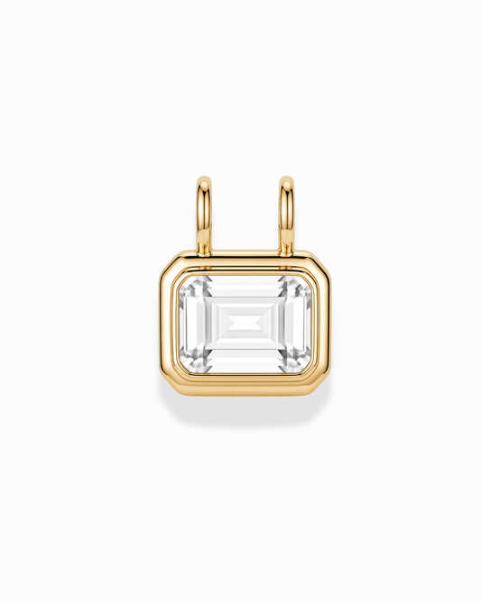 The Elsie Sapphire Bezel Charm by Mod + Jo features an emerald-cut white sapphire set in 14k gold with dual top loops, designed as a pendant, shown against a white background.