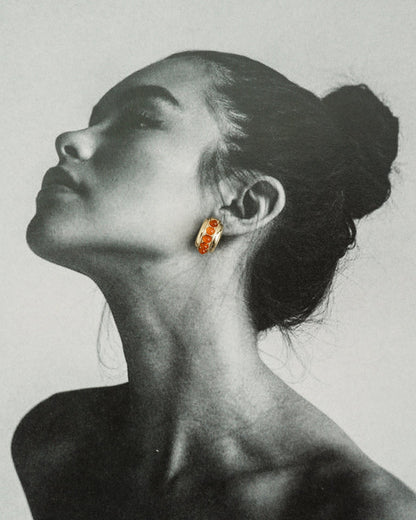 Black and white portrait of a woman with her head tilted back and hair in a bun, wearing Mod + Jo’s Evy Raised Gemstone Hoops—their gold and red gemstones stand out in vibrant color against the grayscale image.