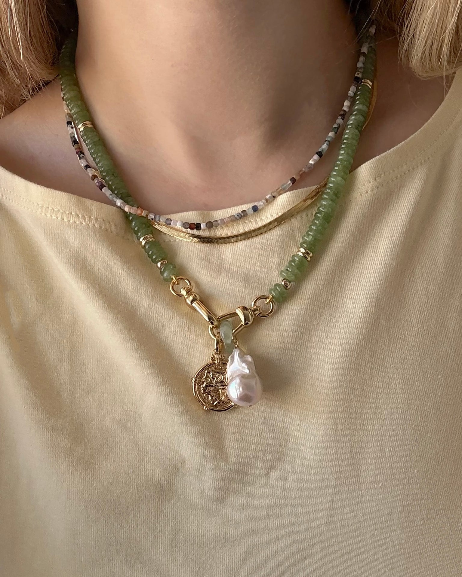 Close-up of a person wearing the Mod + Jo Merit Gemstone Necklace with multicolored beads, layered with a 14k gold-filled pearl and coin pendant, styled over a light yellow tee. All pieces are handmade in Dallas.