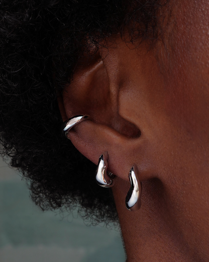Close-up of an ear wearing silver wavy hoop earrings with a blurred background