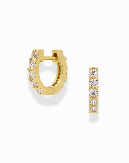 The Mod + Jo Harlow Reversible Birthstone Huggies are small 18k gold plated hoops featuring a row of round, clear gemstones on the front, shown from side and front angles against a white background.