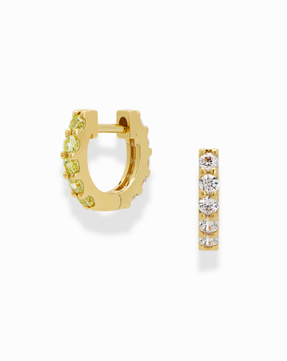 The Harlow Reversible Birthstone Huggies by Mod + Jo are small 18k gold plated hoops, each featuring a row of round sparkling gemstones; one is shown from the side, the other from the front on a white background.