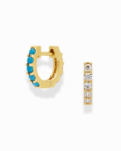 The Harlow Reversible Birthstone Huggies by Mod + Jo feature one gold-plated hoop with turquoise stones and the other with clear crystals, elegantly displayed on a white background.