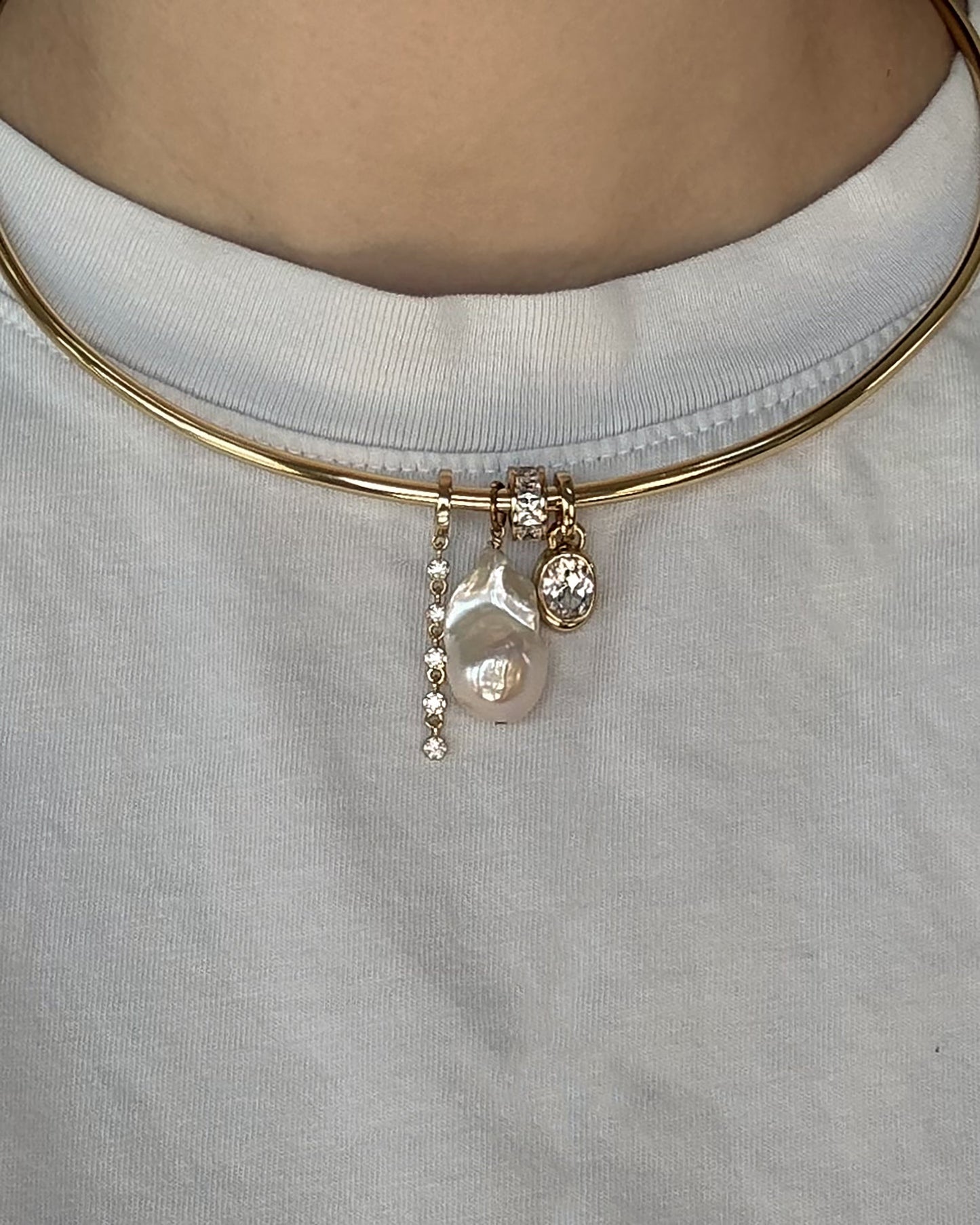 The Demi Tennis Charm choker necklace by Mod + Jo features 14k gold plating and three distinctive pendants—a row of small CZ charms, a large irregular pearl, and a small round crystal—styled here over a white t-shirt.