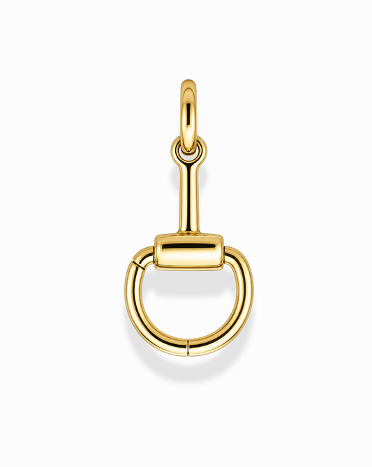 The Paige Horsebit Charm Enhancer by Mod + Jo is a 14k gold-plated, nickel-free, and tarnish-resistant pendant designed in the shape of a snaffle bit, featuring a circular lower section with a straight horizontal bar at the top. Photographed on a plain white background, this piece ensures both elegance and lasting shine.
