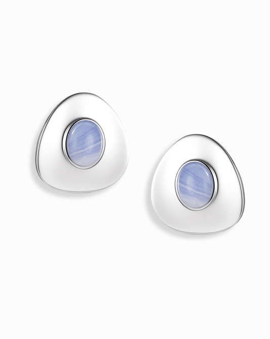The Mod + Jo Hunter Statement Studs are silver triangular earrings with a central round blue chalcedony stone, shown on a white background.