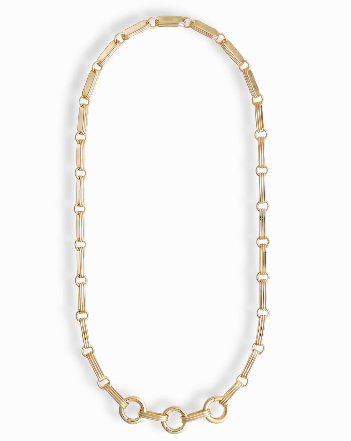 The Jagger Charm Clip Necklace by Mod + Jo features elongated oval links crafted in 14k gold and showcases three larger connected circles at the bottom, elegantly displayed on a white background. This sophisticated necklace seamlessly blends timeless style with contemporary flair.