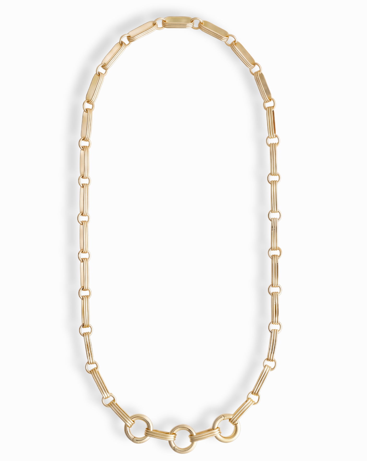 The Jagger Charm Clip Necklace by Mod + Jo features elongated oval links crafted in 14k gold and showcases three larger connected circles at the bottom, elegantly displayed on a white background. This sophisticated necklace seamlessly blends timeless style with contemporary flair.