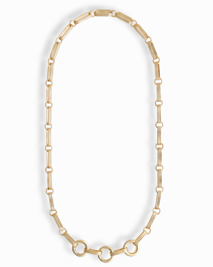 The Jagger Charm Clip Necklace by Mod + Jo features elongated oval links crafted in 14k gold and showcases three larger connected circles at the bottom, elegantly displayed on a white background. This sophisticated necklace seamlessly blends timeless style with contemporary flair.