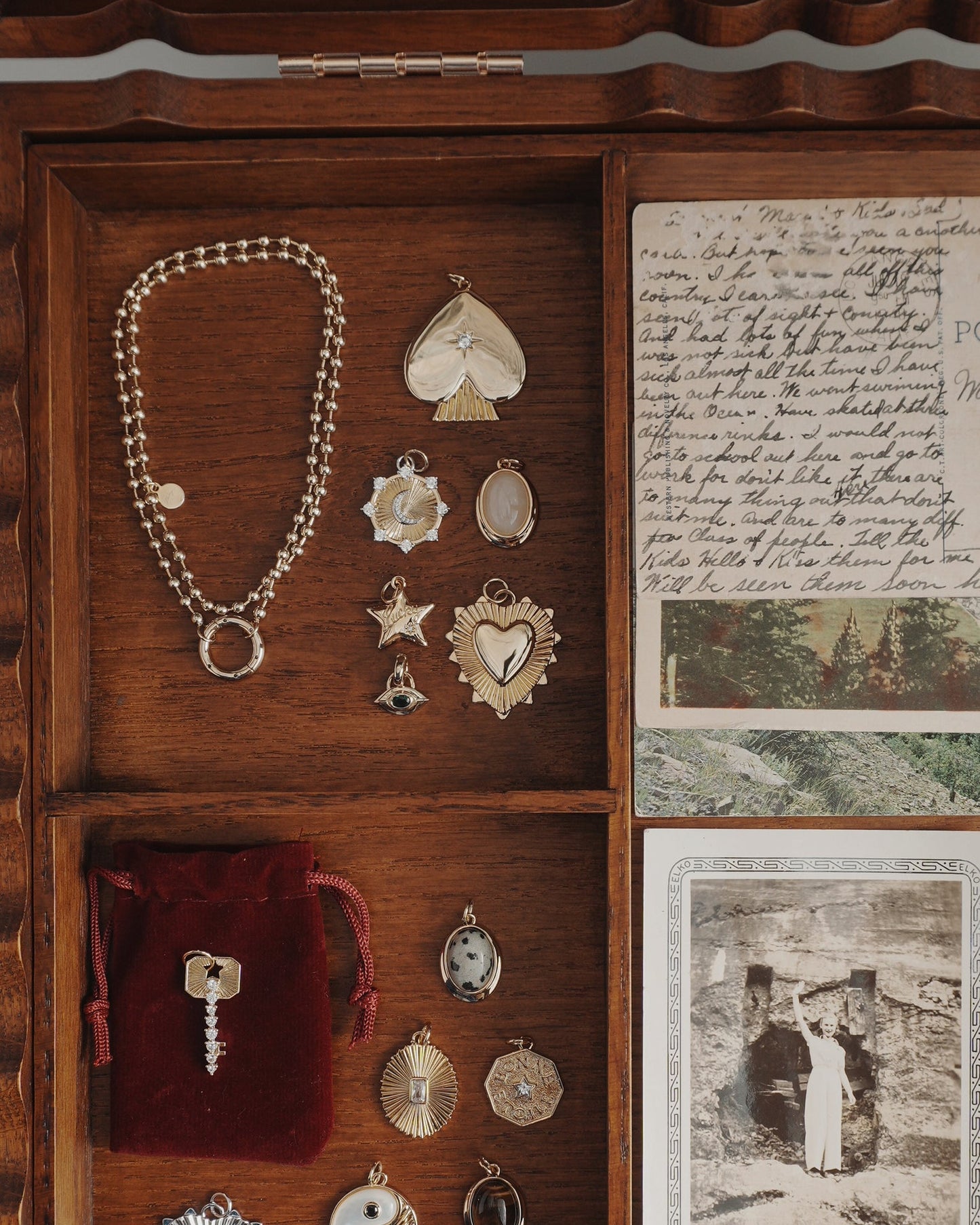A Mod + Jo Veya Spade Charm jewelry box containing 14k gold pendants, charms, a bracelet, a red velvet pouch with a key, handwritten letters, and a black-and-white vintage photo.