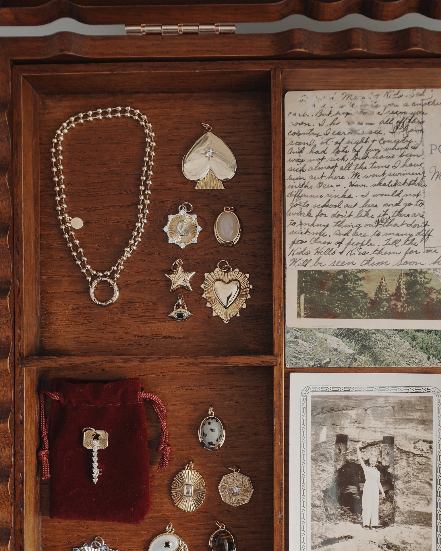 A Mod + Jo Veya Spade Charm jewelry box containing 14k gold pendants, charms, a bracelet, a red velvet pouch with a key, handwritten letters, and a black-and-white vintage photo.