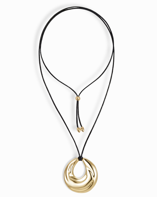 The Mod + Jo Kira Cord Necklace features a black cord with adjustable gold bead fasteners and a bold, shiny abstract gold pendant in an eye-catching circular design.