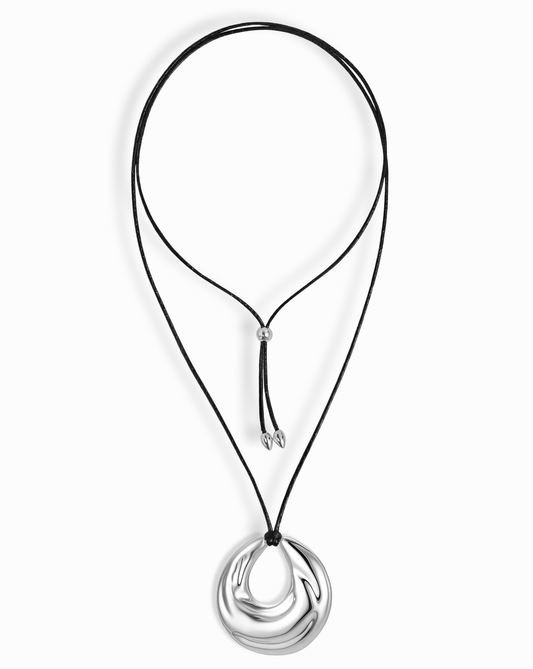 The Kira Cord Necklace by Mod + Jo features a black cord with an adjustable sliding knot and a large, smooth, sculptural gold and silver circular pendant.