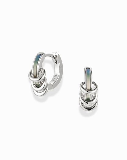 Mod + Jo Levi Huggies: Silver hoop earrings with interlocking ring charms and a blue-grey enamel bar, featuring a tarnish-resistant finish. Shown as a pair against a white background.