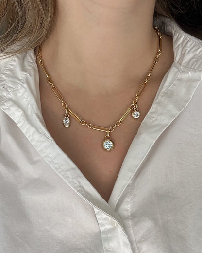 A person wears a white collared shirt and the Mod + Jo Liam Watch Chain Necklace, a vintage-inspired piece with three round, sparkling pendants in tarnish-resistant 14k gold-plating.