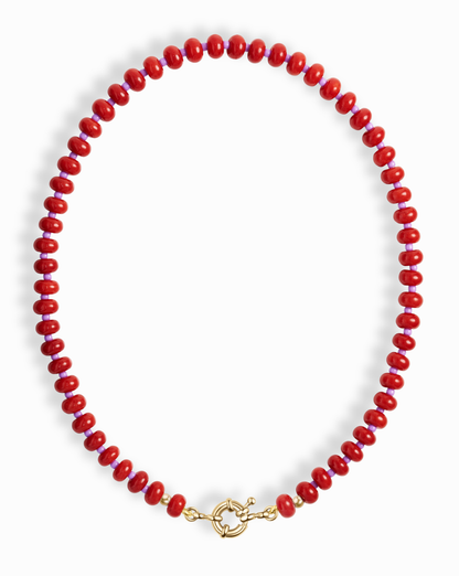 The Macey Gemstone Necklace by Mod + Jo features round, glossy red beads and a gold toggle clasp, artfully displayed in a circular shape on a white background.