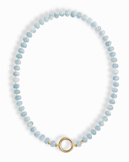 The Macey Gemstone Necklace by Mod + Jo features round, light blue marbled beads and a standout round gold clasp at the front.