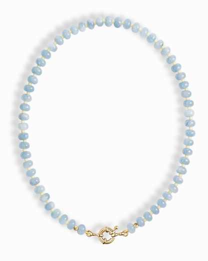 The Macey Gemstone Necklace by Mod + Jo features round light blue and white beads with a gold toggle clasp, displayed in a circle on a white background.