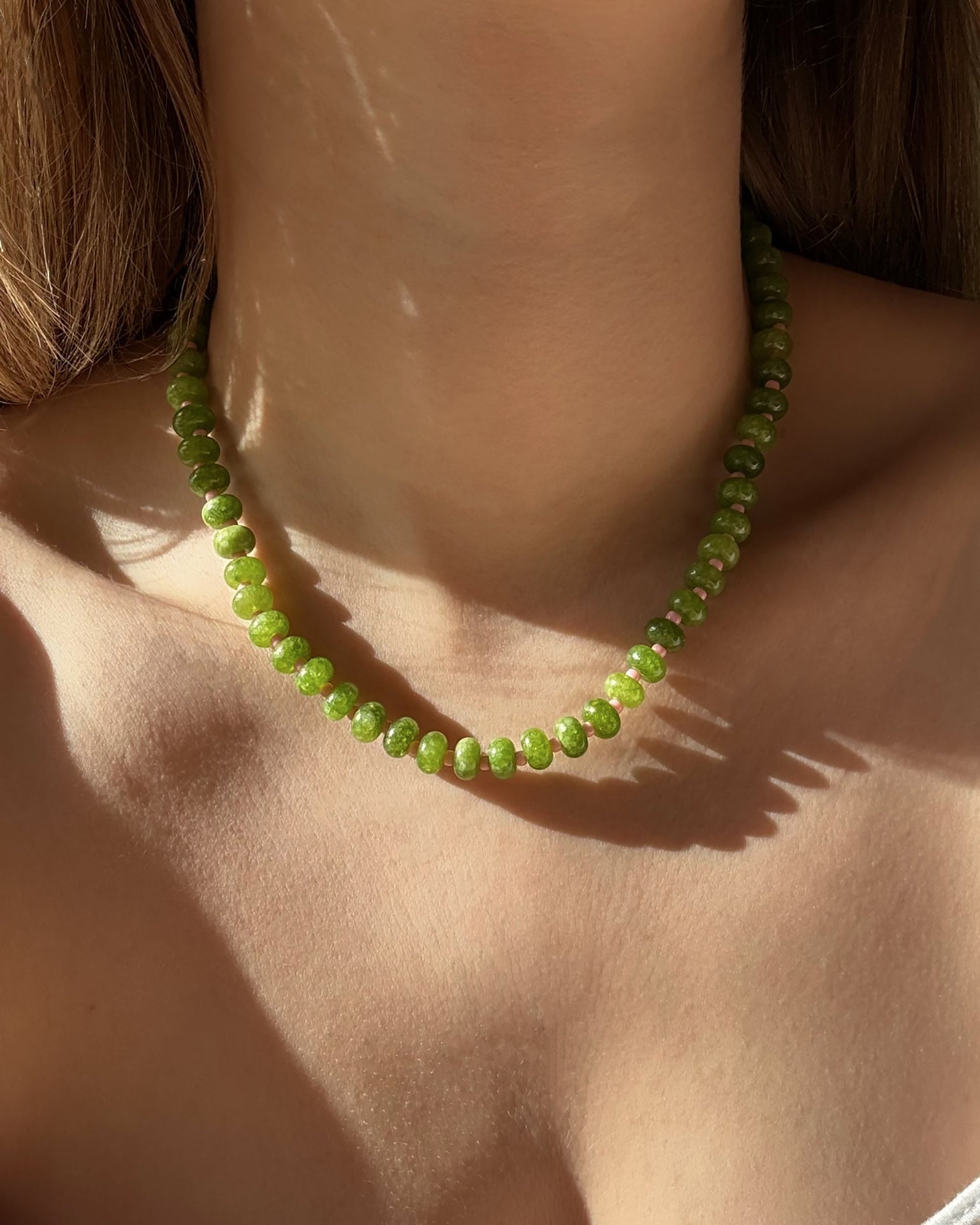 A close-up of a woman’s neck and collarbone wearing the Mod + Jo Macey Gemstone Necklace, with sunlight casting soft shadows on her skin.