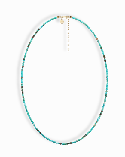 The Merit Gemstone Necklace by Mod + Jo features small, round turquoise beads with subtle color variations, a gold clasp, an adjustable chain, and a small round charm.