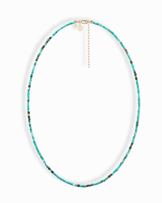 The Merit Gemstone Necklace by Mod + Jo features small, round turquoise beads with subtle color variations, a gold clasp, an adjustable chain, and a small round charm.