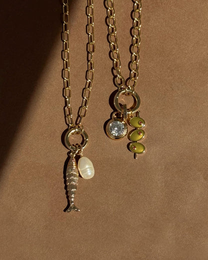 Two Darcy Charm Clip Necklaces by Mod + Jo on a neutral background: one with a paperclip chain, fish and pearl charms; the other with a clear gem and three small green bead charms.
