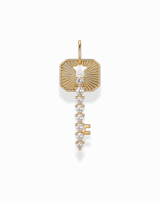 The Noah Key Charm by Mod + Jo is a gold plated, key-shaped pendant embellished with sparkling white gemstones. Featuring a rectangular top with a star-shaped cutout and an intricate, decorative design on a white background, this elegant charm is symbolic jewelry perfect for any occasion.