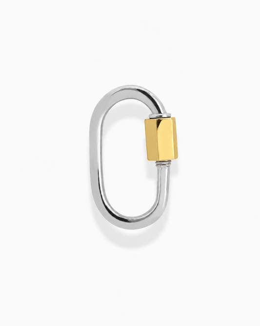 The Mod + Jo Nora Lock Carabiner is a silver, oval-shaped metal clasp with a gold hexagonal screw lock and 14k plating for a tarnish-resistant finish, displayed on a plain white background.