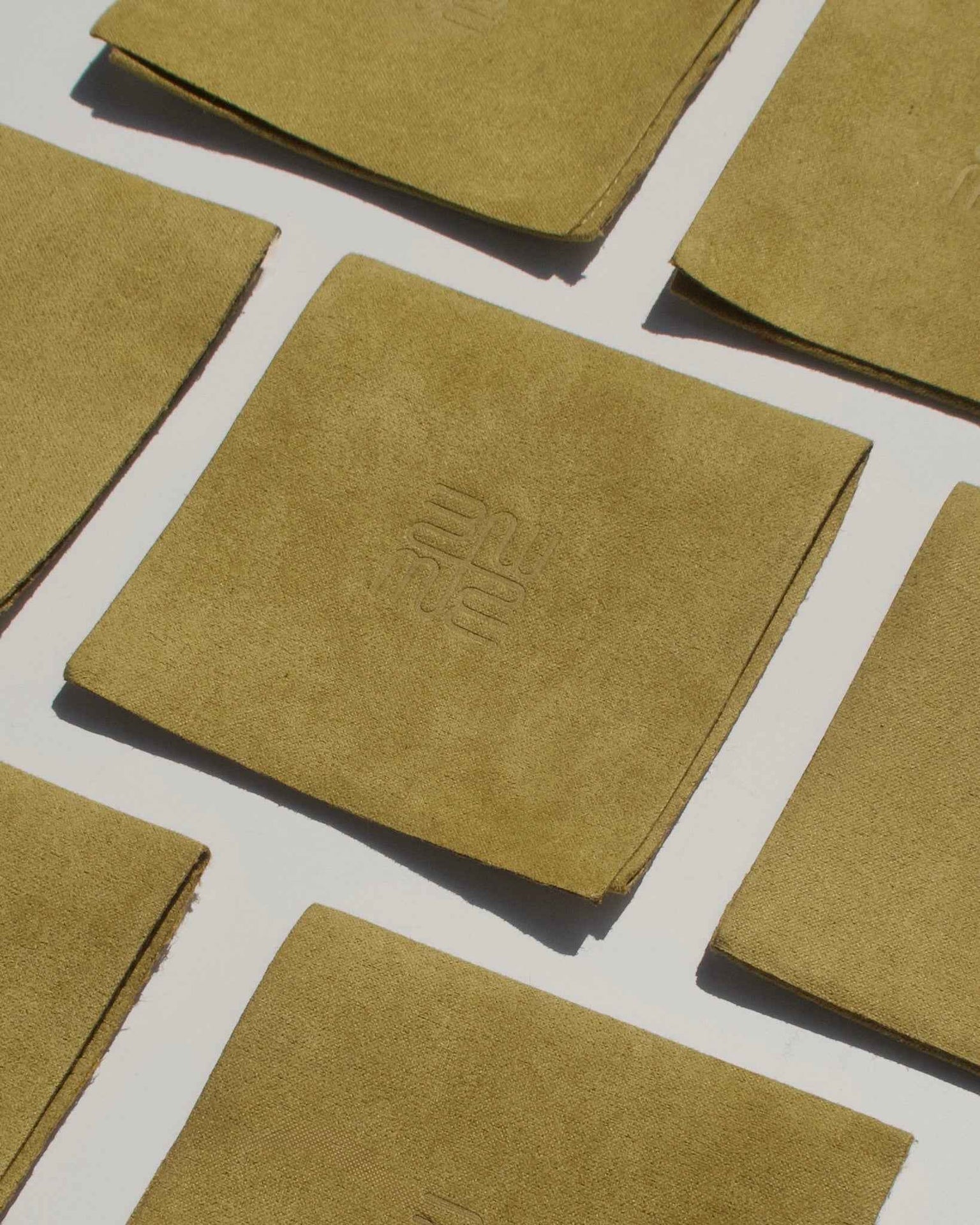 Olive green linen cocktail napkins arranged in a flat lay on white, with the center napkin featuring an embossed monogram. Accented by Mod + Jo Levi Huggies for a tarnish-resistant shine. Photographed in natural light with soft shadows.